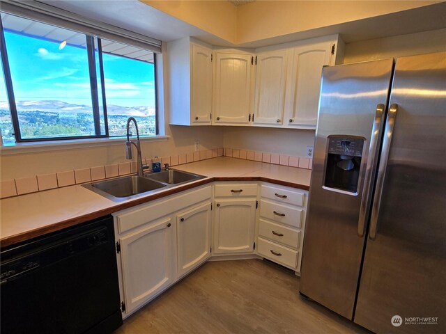 kitchen featuring stainless steel fridge, white cabinetry, sink, black dishwasher, and light hardwood / wood-style floors