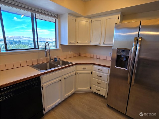 kitchen with white cabinetry, black dishwasher, stainless steel fridge, and a sink