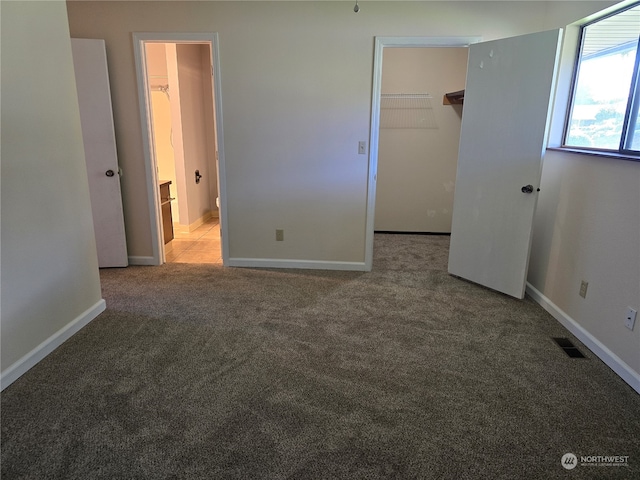 unfurnished bedroom featuring a walk in closet, a closet, and carpet floors