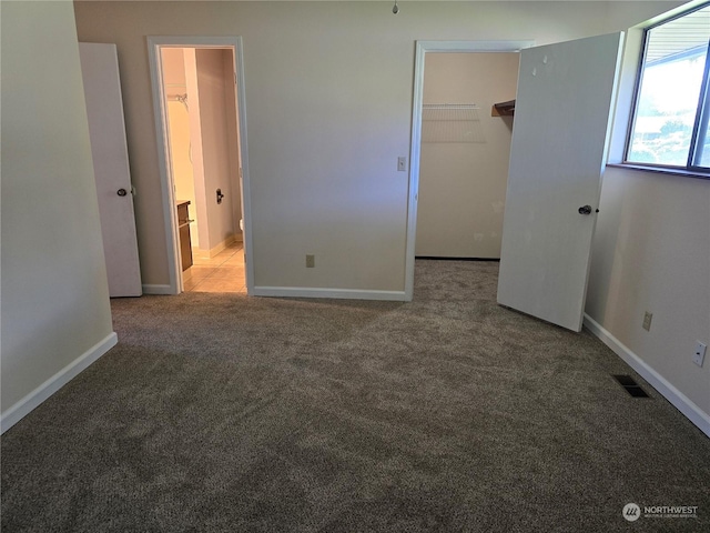 unfurnished bedroom featuring visible vents, a walk in closet, baseboards, light carpet, and a closet