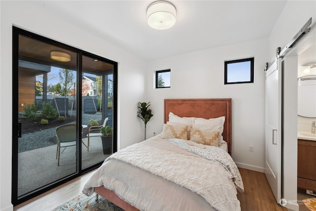 bedroom featuring a barn door, hardwood / wood-style flooring, connected bathroom, and access to exterior