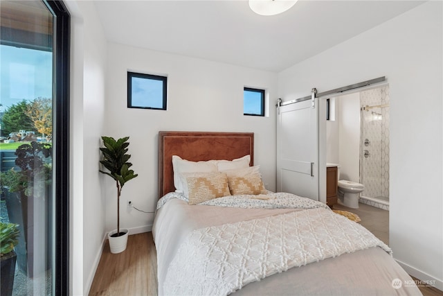 bedroom with a barn door, hardwood / wood-style flooring, and connected bathroom