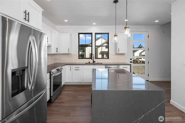 kitchen with appliances with stainless steel finishes, white cabinets, a center island, and pendant lighting