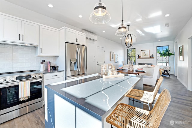 kitchen featuring pendant lighting, a wall mounted AC, white cabinetry, stainless steel appliances, and exhaust hood