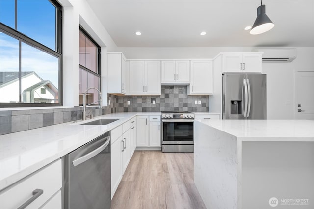 kitchen with appliances with stainless steel finishes, sink, white cabinetry, a wall mounted air conditioner, and hanging light fixtures