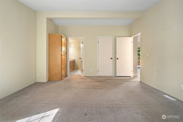 unfurnished bedroom featuring light carpet, ensuite bathroom, and beam ceiling