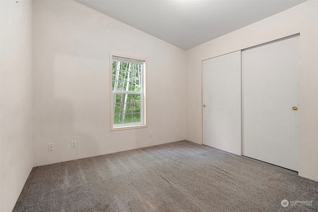 unfurnished bedroom featuring a closet, carpet flooring, a textured ceiling, and vaulted ceiling