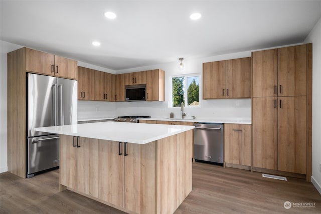 kitchen with light wood-type flooring, a kitchen island, sink, a breakfast bar, and appliances with stainless steel finishes