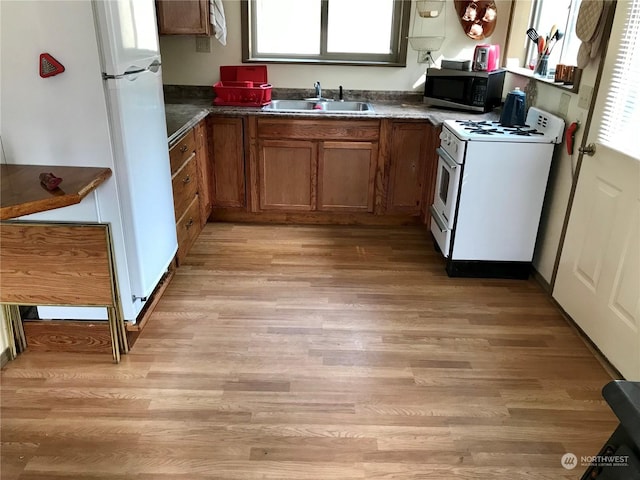 kitchen with a sink, dark countertops, white appliances, light wood-style floors, and brown cabinets