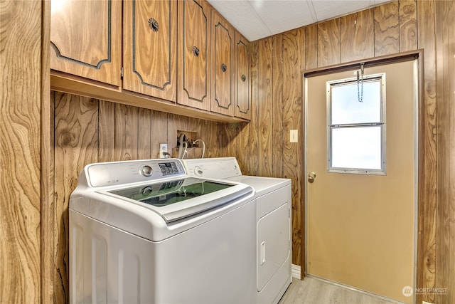 laundry room featuring washer and dryer, cabinets, wood walls, and light hardwood / wood-style flooring