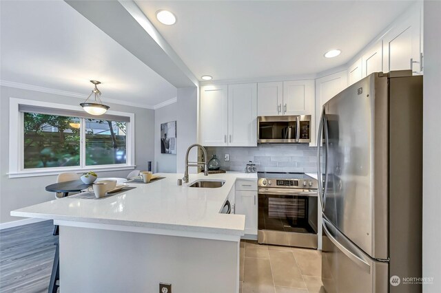 kitchen with sink, appliances with stainless steel finishes, white cabinetry, a kitchen bar, and kitchen peninsula