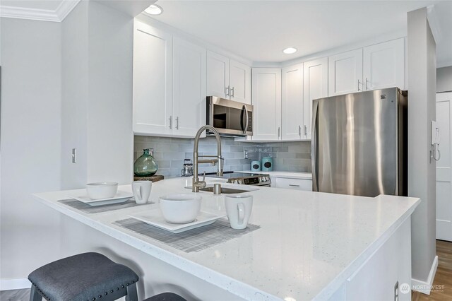 kitchen featuring dark wood-type flooring, a kitchen bar, white cabinetry, stainless steel appliances, and decorative backsplash