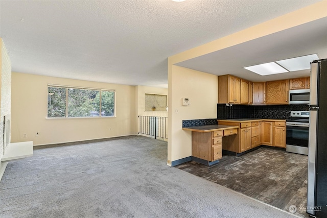 kitchen featuring a textured ceiling, a skylight, dark carpet, stainless steel appliances, and decorative backsplash