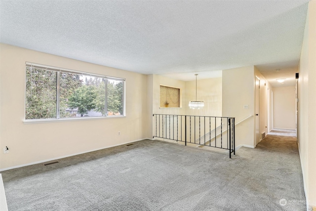 carpeted spare room with a chandelier and a textured ceiling