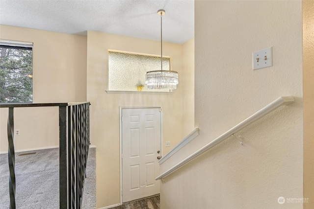 carpeted entrance foyer with a textured ceiling and a notable chandelier