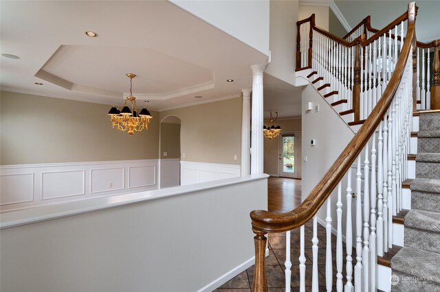 staircase with an inviting chandelier, decorative columns, crown molding, and a tray ceiling