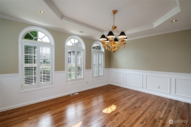 unfurnished dining area featuring ornamental molding, a notable chandelier, a tray ceiling, and hardwood / wood-style floors