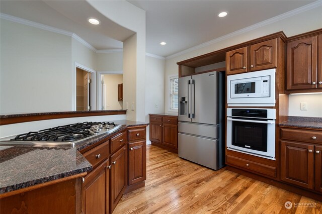 kitchen with appliances with stainless steel finishes, light wood-type flooring, dark stone countertops, and crown molding