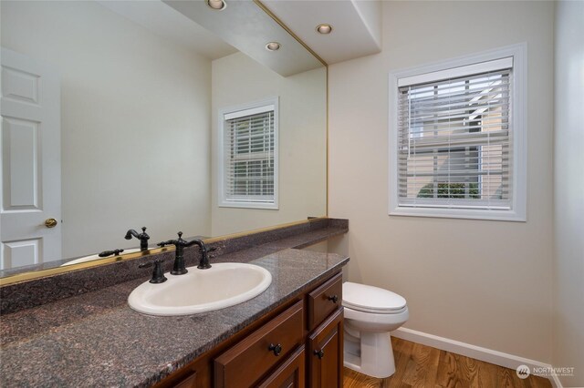 bathroom with toilet, wood finished floors, recessed lighting, baseboards, and vanity