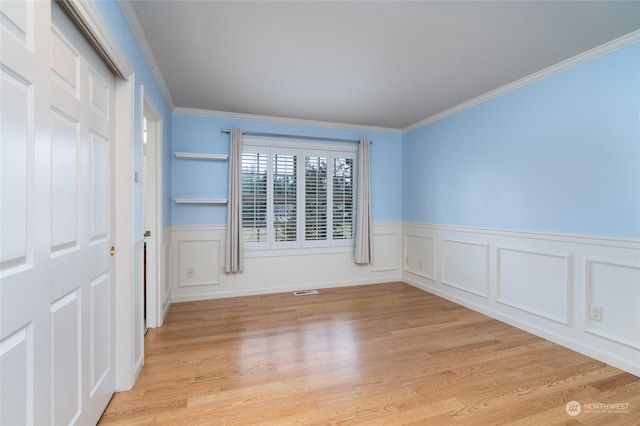 unfurnished room with light wood-type flooring, wainscoting, and crown molding