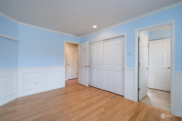 unfurnished bedroom featuring a closet, a wainscoted wall, crown molding, and light wood-style floors