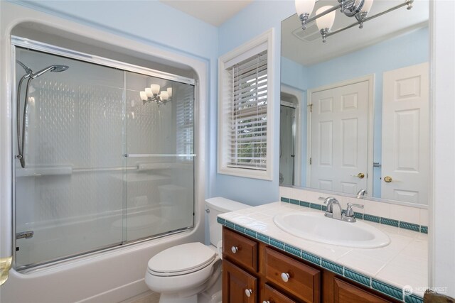 bathroom featuring toilet, vanity, an inviting chandelier, and shower / bath combination with glass door