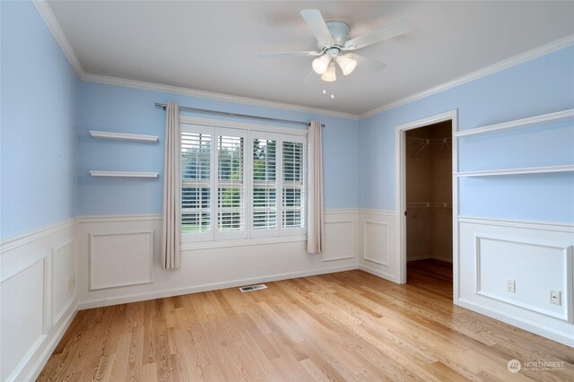 spare room featuring visible vents, a wainscoted wall, a ceiling fan, wood finished floors, and crown molding