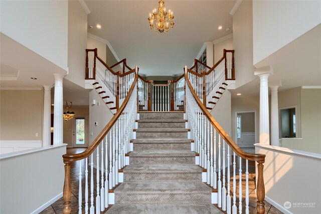 stairway with a high ceiling, a notable chandelier, crown molding, and ornate columns