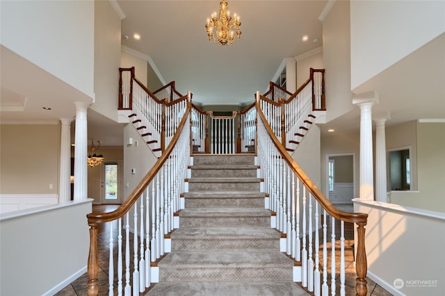 stairs with crown molding, a high ceiling, a notable chandelier, and ornate columns