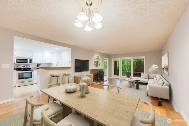 dining area featuring a notable chandelier, light hardwood / wood-style flooring, a textured ceiling, and sink