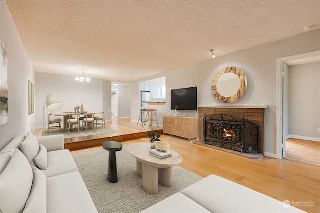 living room featuring a brick fireplace, a notable chandelier, wood-type flooring, and a textured ceiling