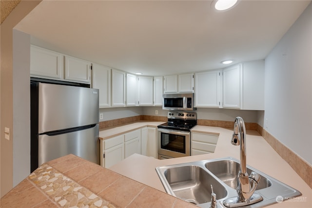 kitchen with sink, tile counters, kitchen peninsula, white cabinets, and appliances with stainless steel finishes