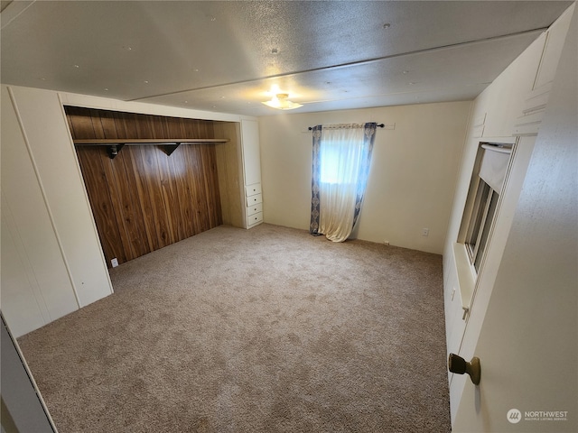 unfurnished bedroom with a closet, wooden walls, a textured ceiling, and carpet floors