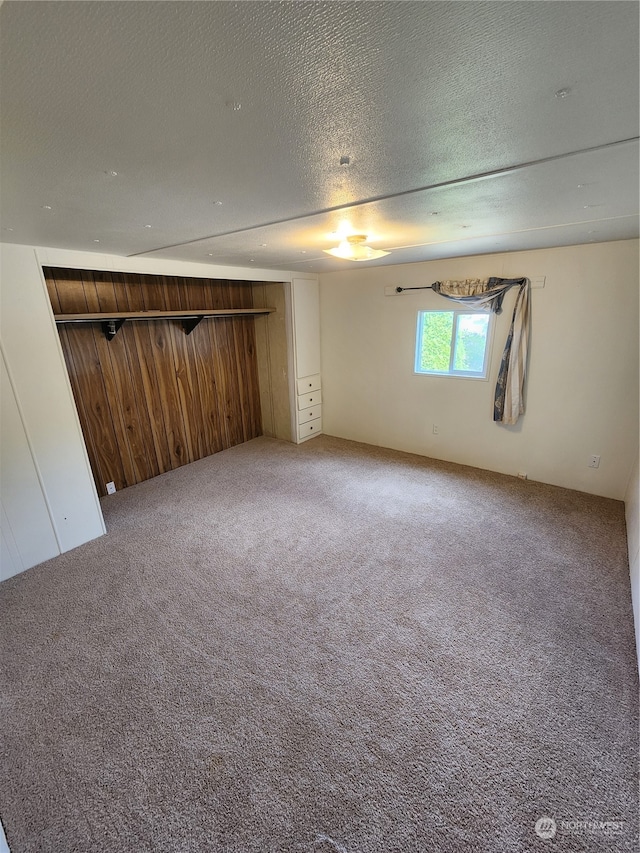 carpeted spare room with wood walls and a textured ceiling