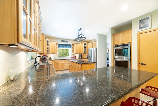 kitchen with dark stone countertops, decorative light fixtures, kitchen peninsula, sink, and appliances with stainless steel finishes