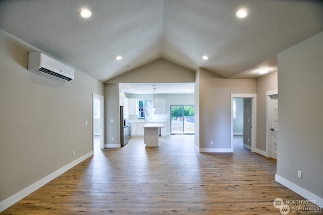 unfurnished living room featuring lofted ceiling, a textured ceiling, hardwood / wood-style flooring, and a wall mounted air conditioner