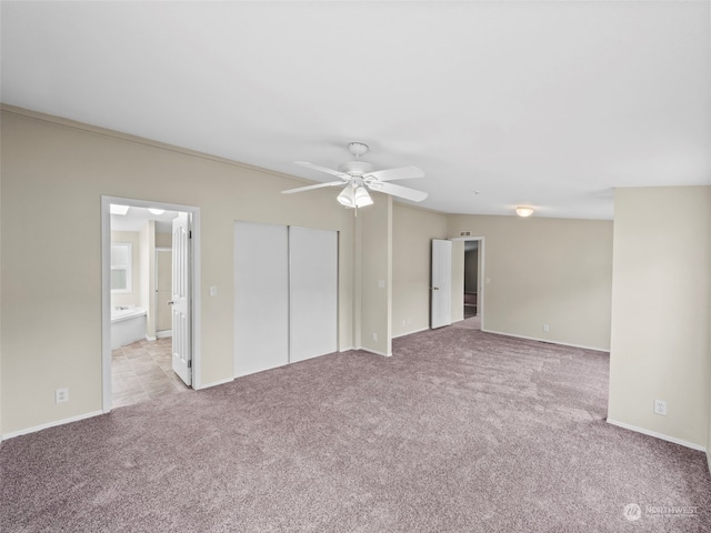 unfurnished bedroom with light carpet, ceiling fan, a closet, and ensuite bath