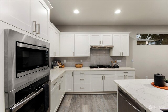 kitchen with stainless steel appliances, light wood-style floors, white cabinetry, decorative backsplash, and under cabinet range hood