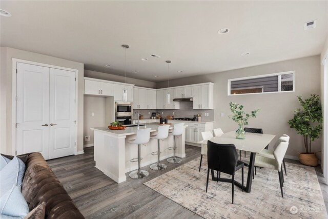 kitchen with a center island with sink, hanging light fixtures, a breakfast bar, hardwood / wood-style flooring, and white cabinets