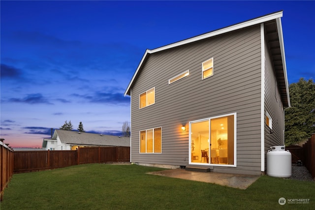 back house at dusk featuring a yard and a patio