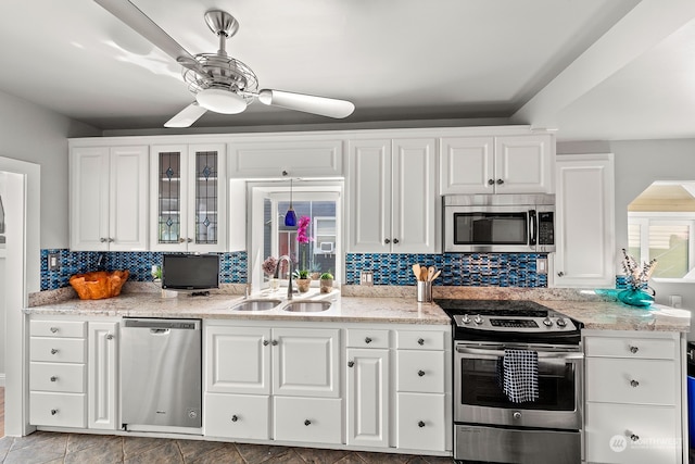 kitchen with appliances with stainless steel finishes, light stone countertops, white cabinetry, sink, and ceiling fan