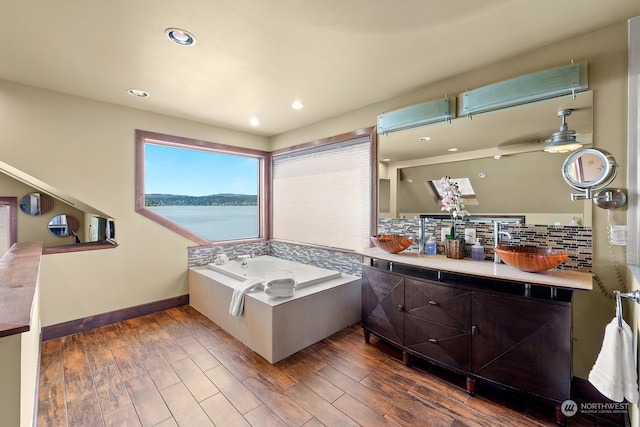 bathroom featuring a water view, wood-type flooring, a tub, and tasteful backsplash