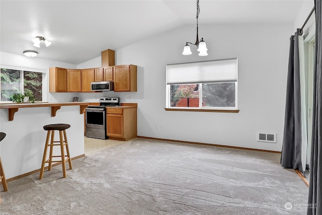 kitchen with a kitchen breakfast bar, an inviting chandelier, pendant lighting, appliances with stainless steel finishes, and lofted ceiling