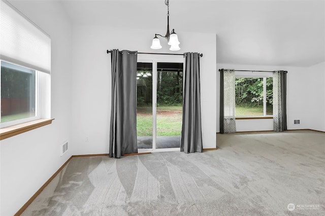 spare room with a wealth of natural light, carpet, and an inviting chandelier