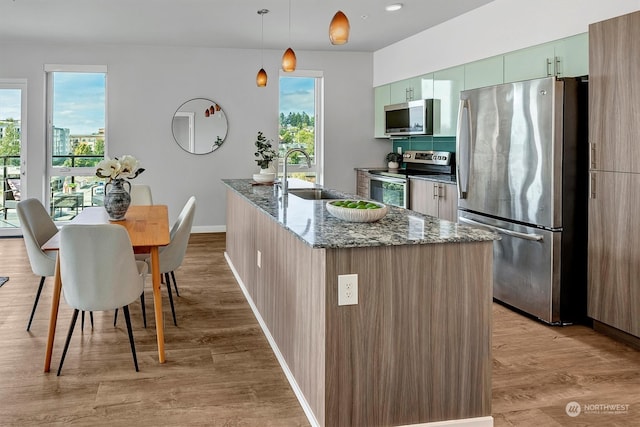 kitchen with stainless steel appliances, light wood-type flooring, decorative light fixtures, sink, and green cabinets