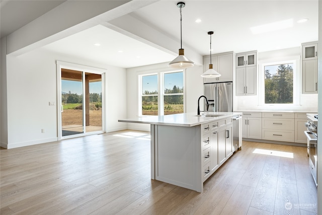 kitchen with decorative light fixtures, a center island with sink, appliances with stainless steel finishes, light wood-type flooring, and white cabinets