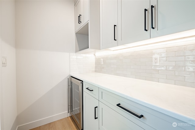 kitchen with wine cooler, light stone countertops, backsplash, light hardwood / wood-style floors, and white cabinetry