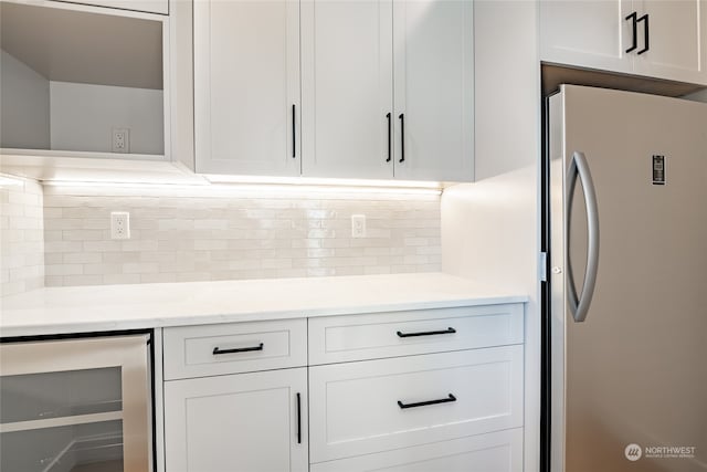 kitchen with beverage cooler, stainless steel fridge, decorative backsplash, and white cabinets