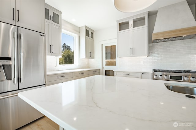 kitchen featuring custom range hood, appliances with stainless steel finishes, light stone countertops, white cabinetry, and decorative backsplash