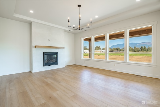 unfurnished living room featuring a raised ceiling, a mountain view, an inviting chandelier, a fireplace, and light hardwood / wood-style floors